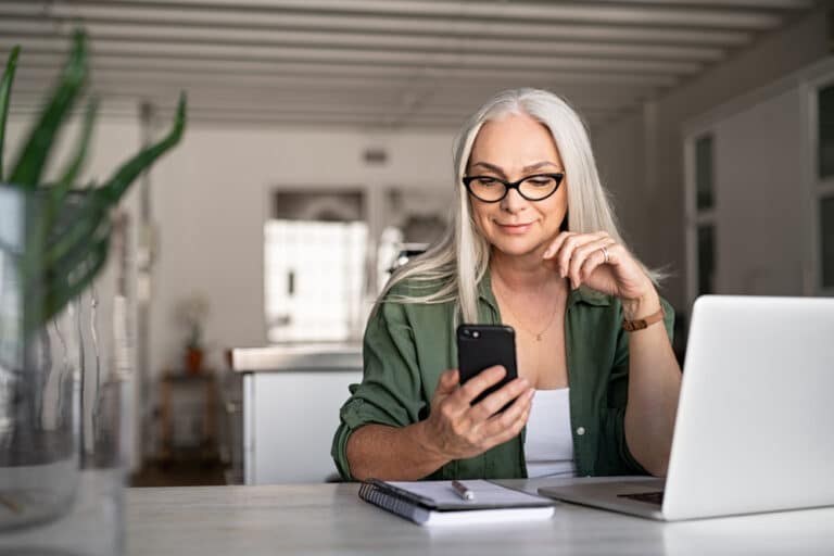 Woman looking at her phone sitting behind a lap top computer