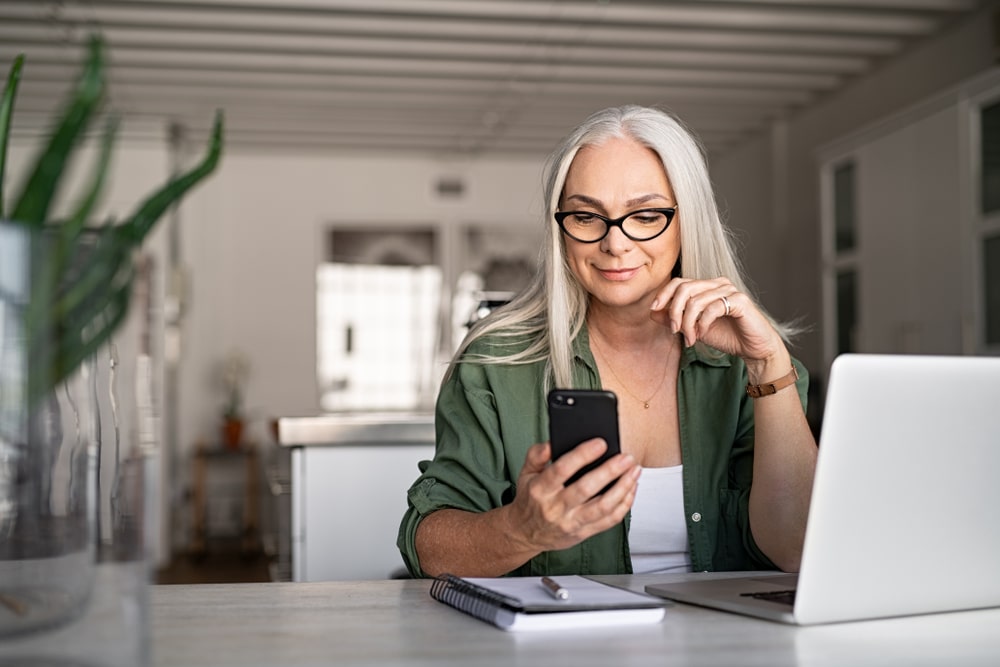 Woman looking at her phone sitting behind a lap top computer