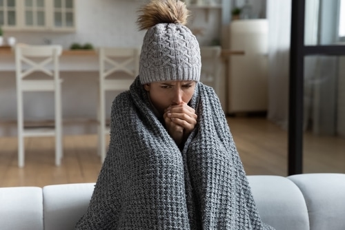 Woman wearing a hat and blanket in a cold house without electricity