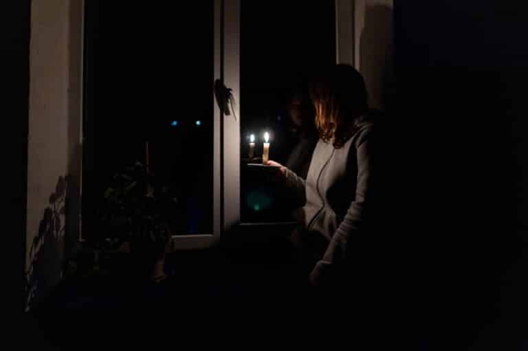 Woman looking out a window holding a candle during a power outage
