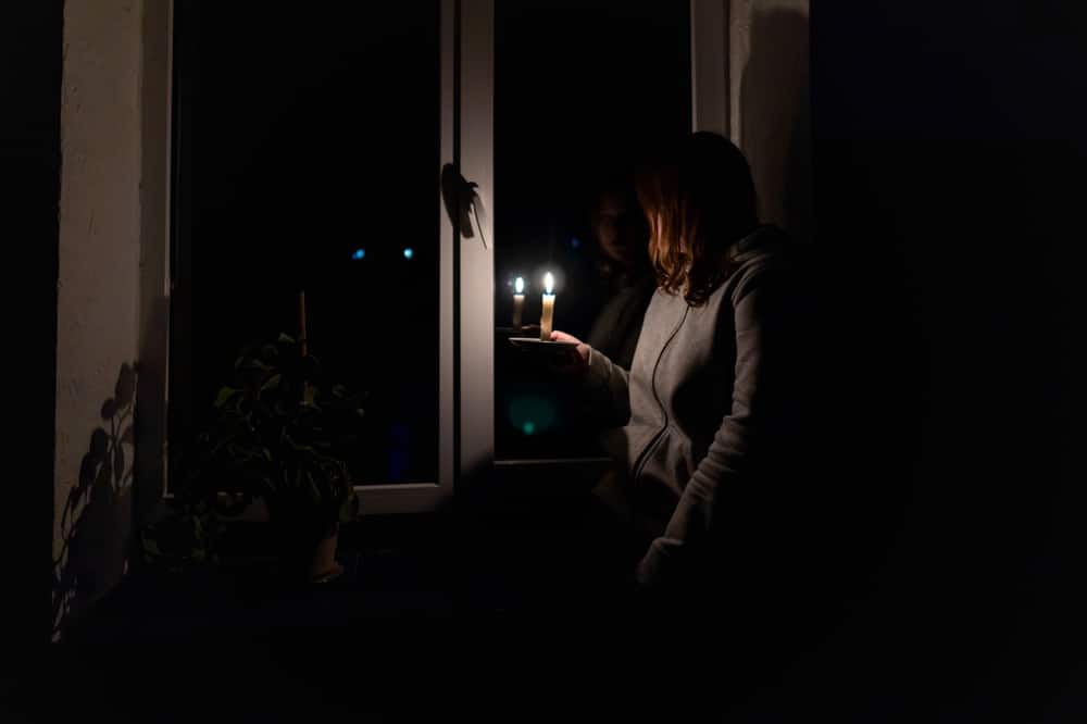Woman looking out a window holding a candle during a power outage
